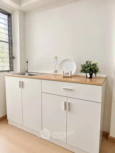 Modern minimalist kitchen with sleek white cabinets and wooden countertop, perfect for compact spaces.