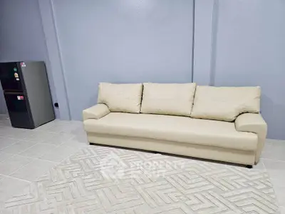 Spacious living room with modern beige sofa and sleek mini fridge on tiled floor.
