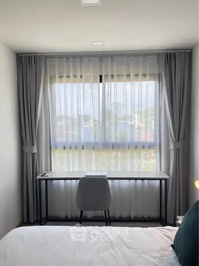 Modern bedroom with study desk and large window, featuring elegant curtains and a comfortable chair.