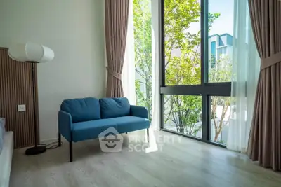 Bright living room with large windows and modern blue sofa, offering a serene view of greenery outside.