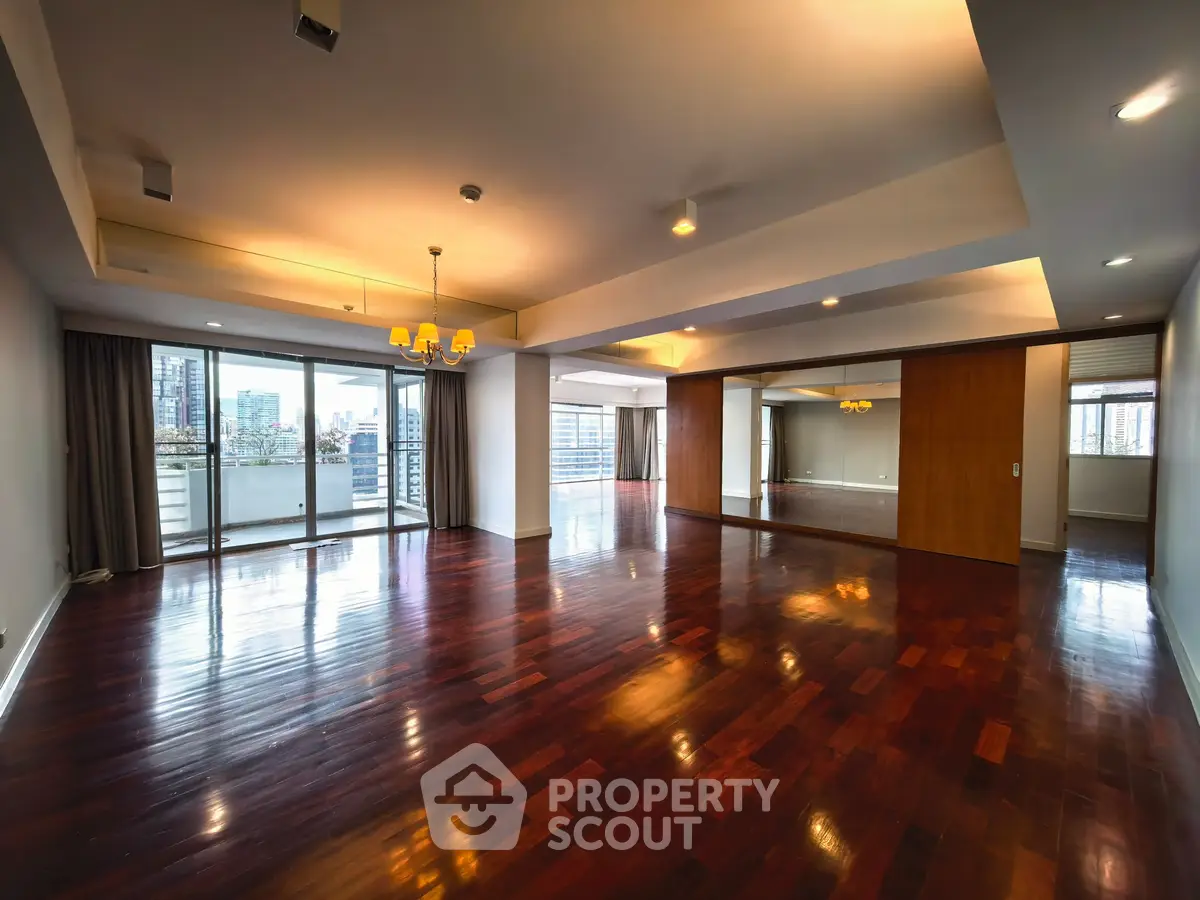 Spacious open-plan living room with hardwood floors and city view balcony.