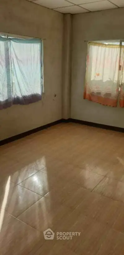 Spacious empty room with tiled flooring and natural light through curtained windows.