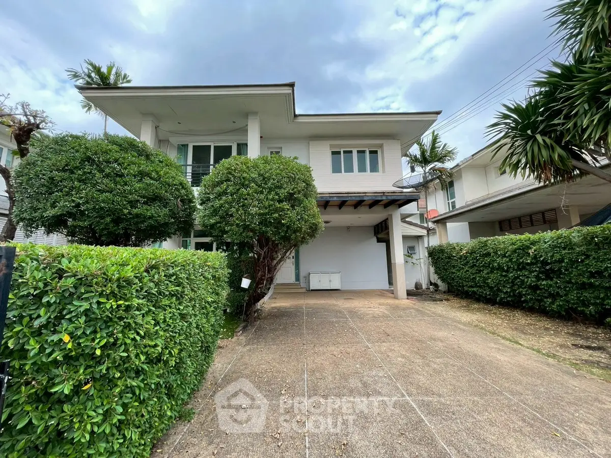 Charming two-story house with lush greenery and spacious driveway in a serene neighborhood.