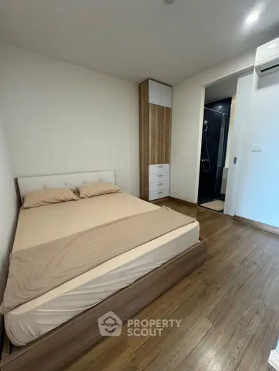 Modern bedroom with wooden flooring and ensuite bathroom in a stylish apartment.