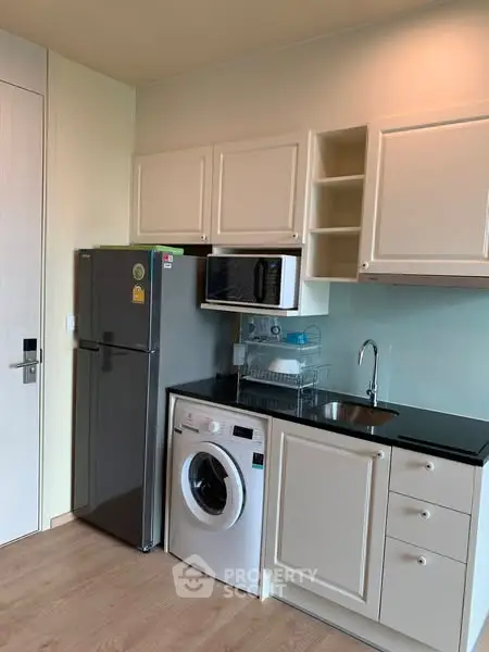 Modern kitchen with sleek appliances and compact design, featuring washing machine and microwave.