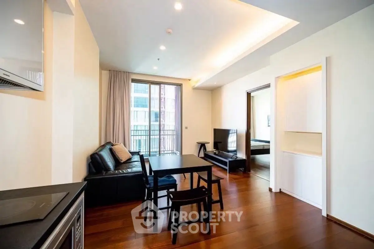 Modern living room with open layout and balcony access, featuring sleek furniture and wooden flooring.