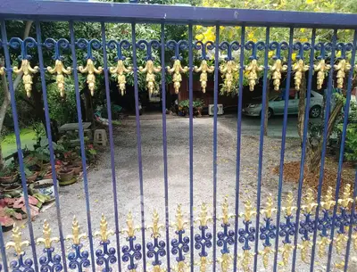 Charming gated entrance with lush garden and driveway leading to a cozy home.