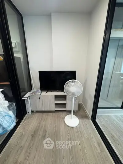 Modern small living room with TV and fan, featuring sleek wooden flooring and glass partitions.
