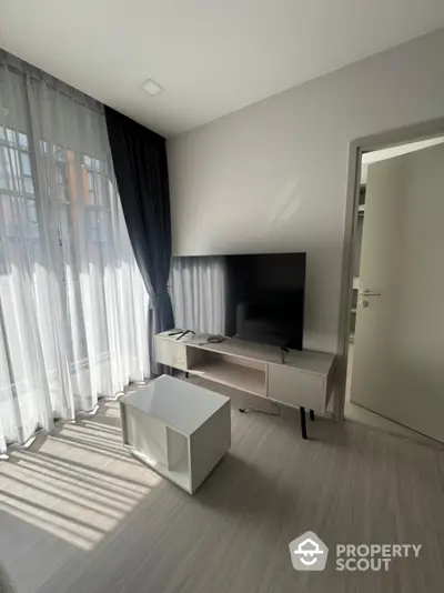 Modern living room with large TV and natural light from floor-to-ceiling windows.