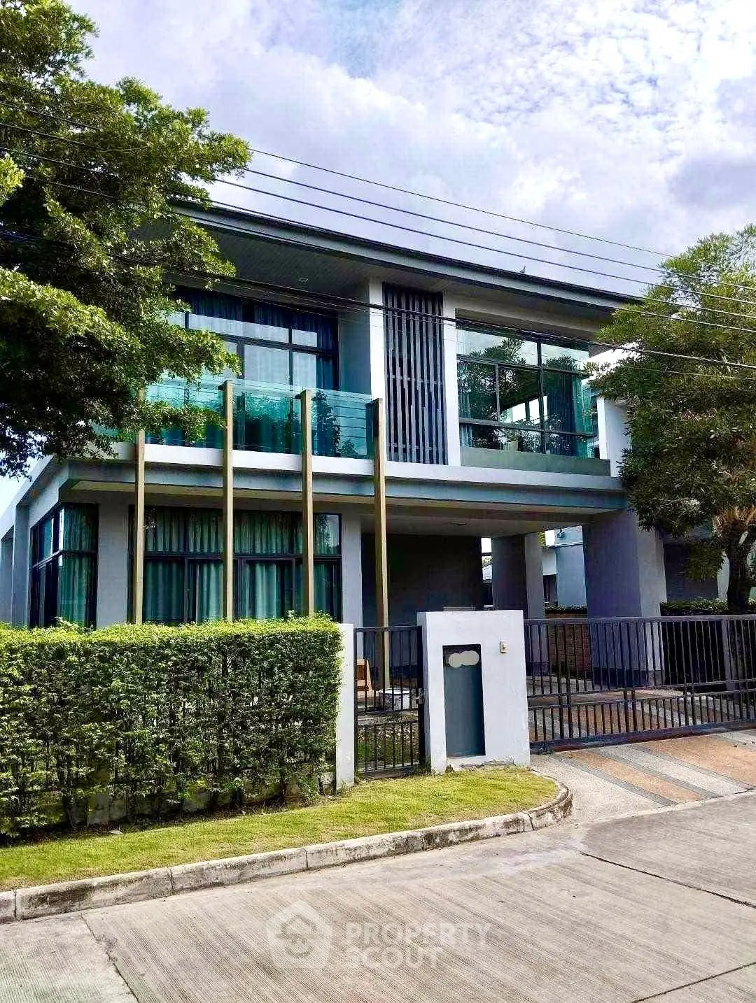 Modern two-story house with large windows and lush greenery in a serene neighborhood.