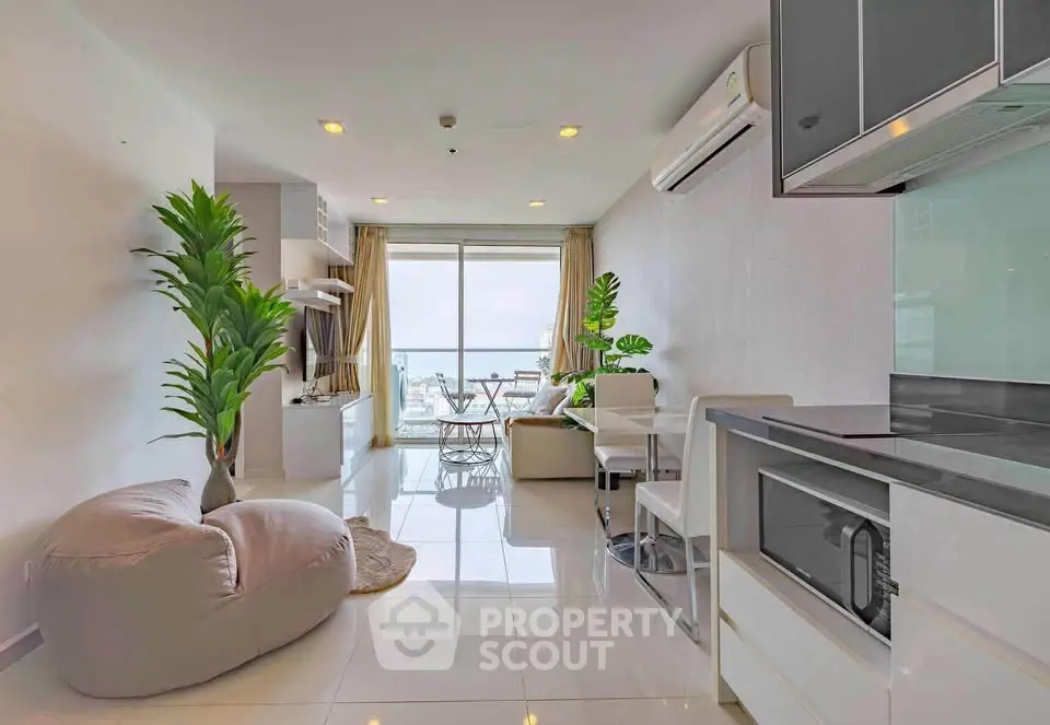 Modern living room with open kitchen and stunning city view, featuring sleek furniture and abundant natural light.