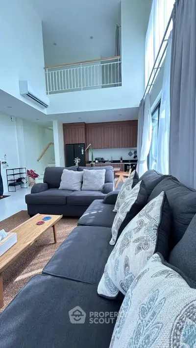 Spacious modern living room with high ceilings and elegant decor, featuring a cozy seating area and open kitchen.