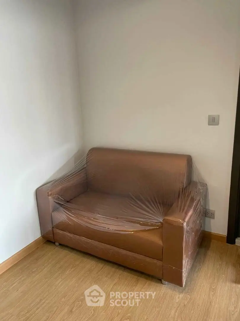 Cozy small sofa wrapped in plastic in a minimalistic room with wooden flooring.