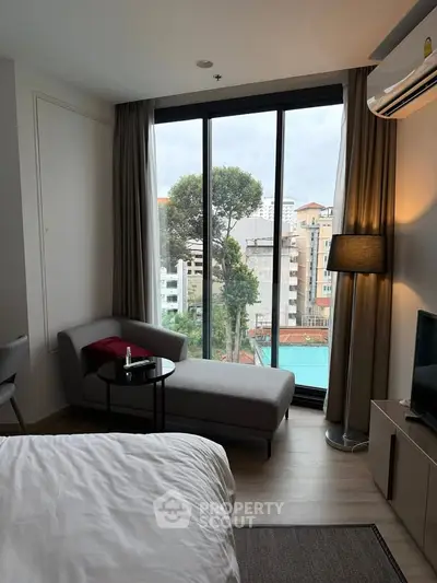 Modern bedroom with large window offering city view, featuring stylish furniture and cozy ambiance.