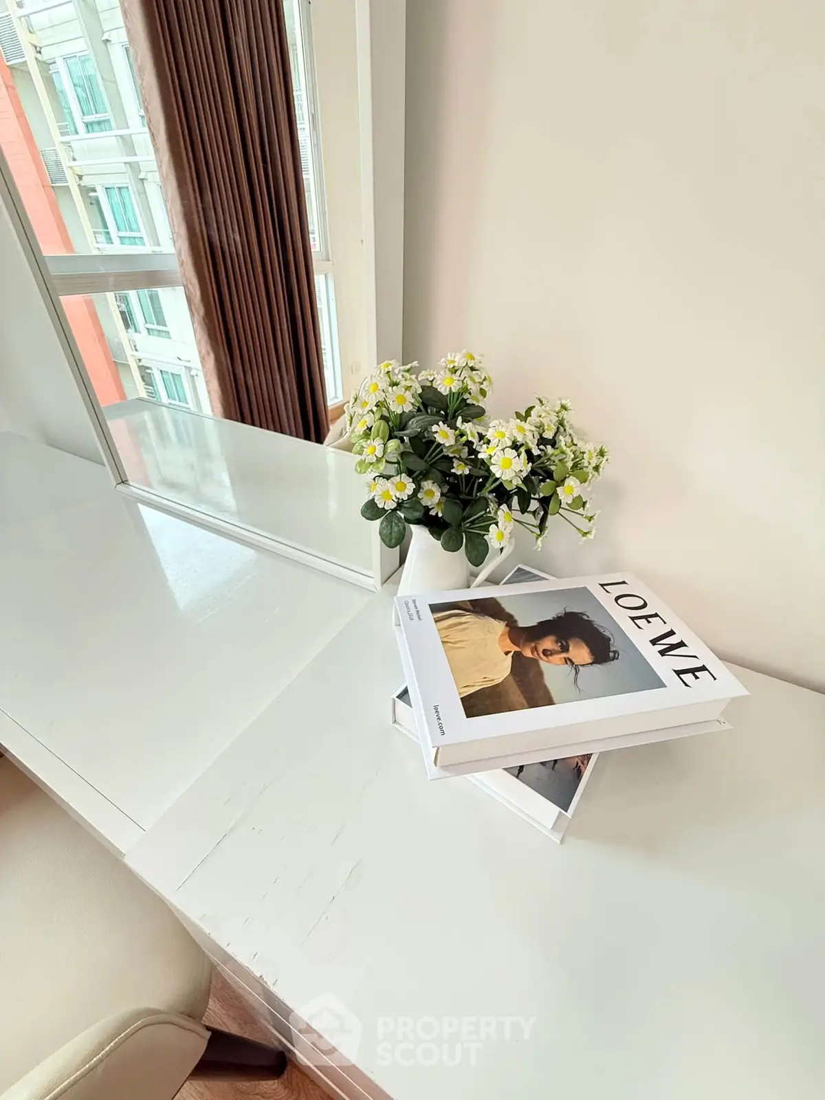 Bright study area with white desk and decorative books near window with city view.