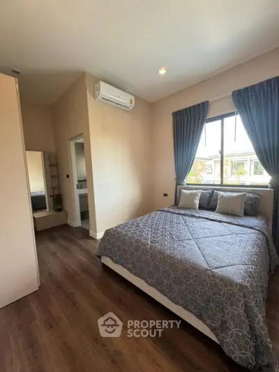 Spacious bedroom with polished wooden flooring, large windows with elegant drapes, and a modern air conditioning unit, offering a serene and comfortable living space.