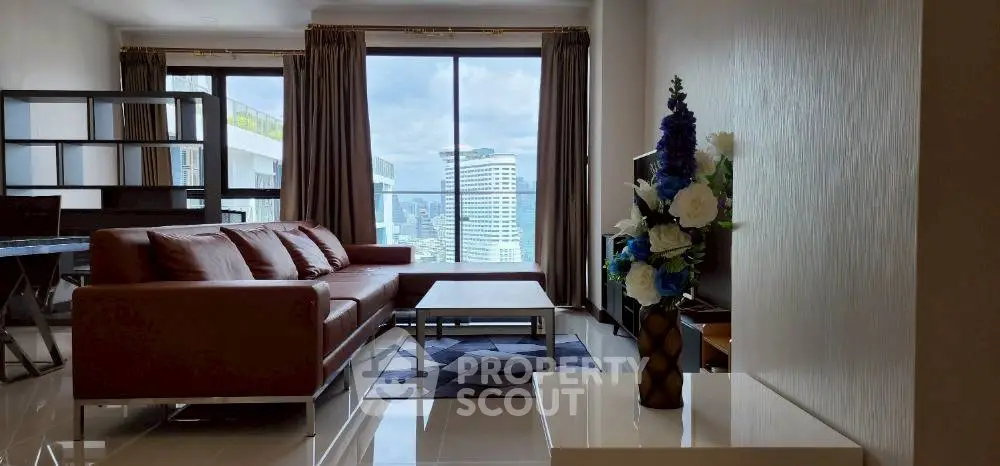 Spacious living room with modern decor and city view, featuring a stylish brown sofa and elegant floral arrangement.