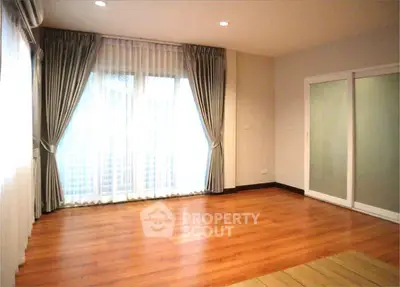 Spacious empty room with wooden flooring and large windows, ideal for customization.