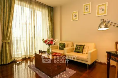 Elegant living room with cozy seating and floral decor, featuring large windows and wooden flooring.