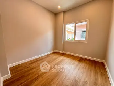Spacious empty room with wooden flooring and large window in modern home.