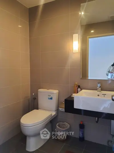 Modern bathroom with sleek fixtures and neutral tiles, featuring a wall-mounted sink and contemporary lighting.