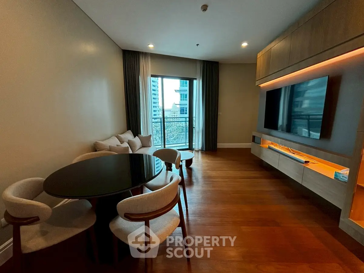 Modern living room with sleek furniture and large TV, featuring a cozy dining area and balcony view.