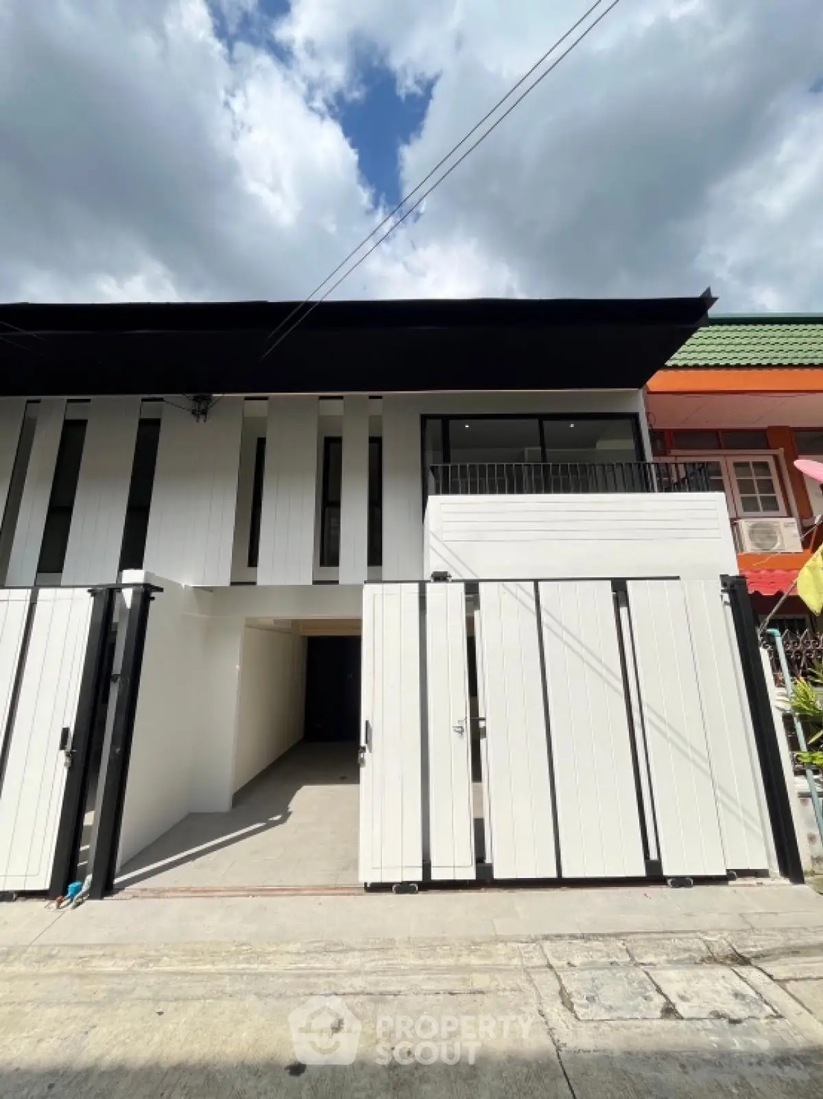 Modern two-story townhouse with sleek facade and gated entrance under a clear blue sky.
