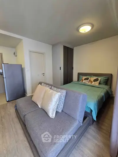Modern studio apartment with cozy bed and stylish sofa, featuring sleek wooden flooring and contemporary lighting.