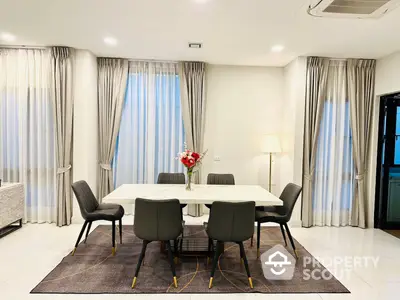 Spacious and elegantly furnished dining area with a large table, comfortable chairs, and floor-to-ceiling curtains enhancing the room's luxurious feel.