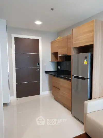 Modern kitchen with sleek wooden cabinets and stainless steel fridge in stylish apartment.
