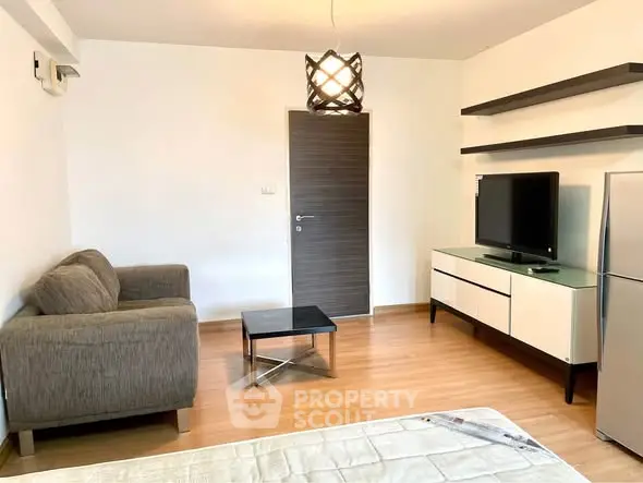 Modern living room with stylish furniture and TV, featuring wooden flooring and contemporary lighting.