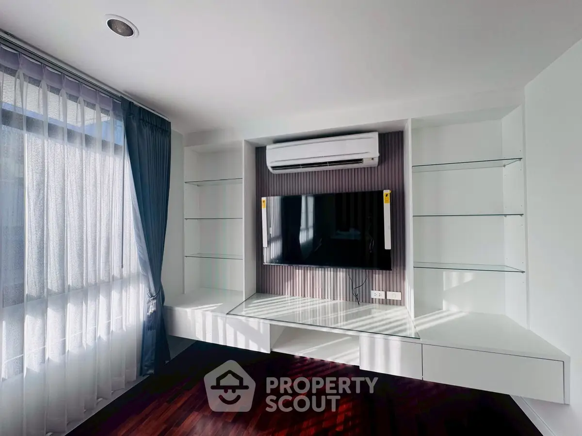 Modern living room with built-in TV unit and air conditioning, featuring elegant sheer curtains and hardwood floors.