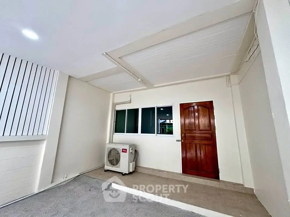 Spacious covered parking area with air conditioning unit and wooden door entry.