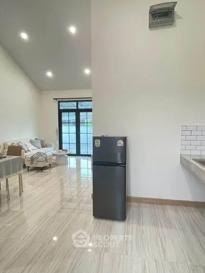 Modern open-plan living room with sleek kitchen and stylish furniture, featuring a stainless steel fridge.