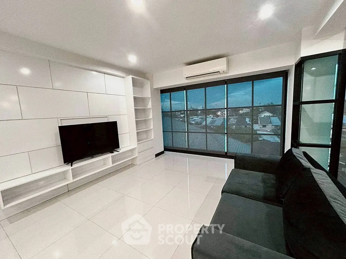 Modern living room with sleek design, large windows, and city view, featuring a TV and comfortable seating.