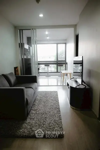 Modern living room with large windows and balcony view, featuring cozy gray sofa and sleek TV stand.