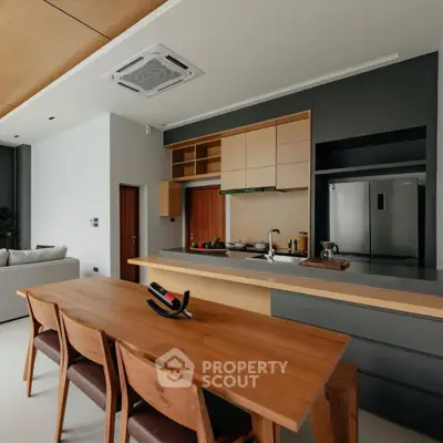 Modern kitchen with sleek design, featuring wooden dining table and stainless steel appliances.
