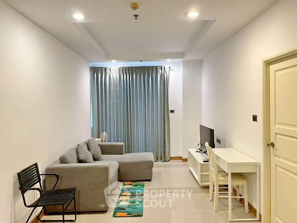 Modern living room with cozy gray sofa, sleek TV setup, and elegant curtains in a bright apartment.