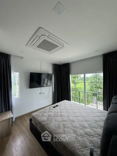 Spacious bedroom with large windows and balcony view, featuring modern ceiling air conditioning.