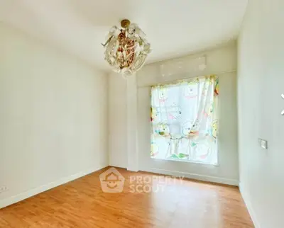 Spacious empty room with wooden flooring and decorative ceiling light.