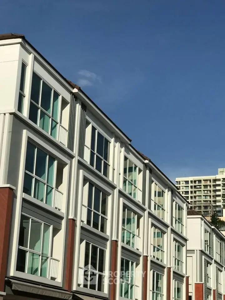 Modern multi-story residential building with large windows and clear blue sky backdrop.