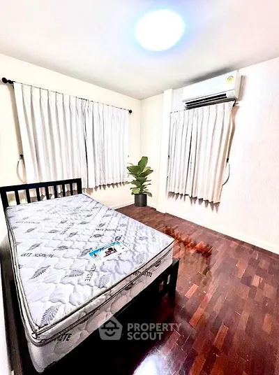 Spacious bedroom with wooden flooring and air conditioning, featuring a comfortable bed and natural light.