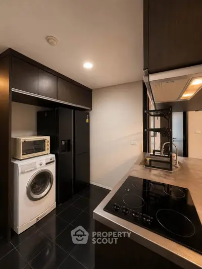 Modern kitchen with sleek appliances and dark cabinetry, featuring a washing machine and electric cooktop.