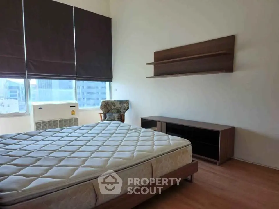 Spacious bedroom with large windows and modern furniture in a high-rise apartment.