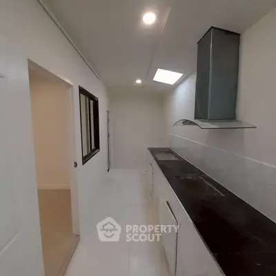 Modern kitchen with sleek design and skylight, featuring a long countertop and built-in stove.