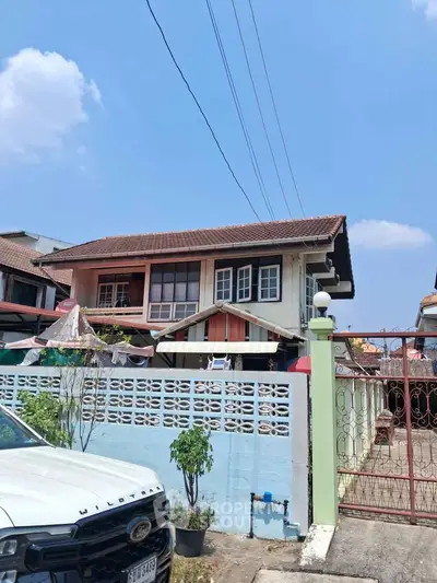 Charming two-story house with a tiled roof and gated entrance in a suburban neighborhood.