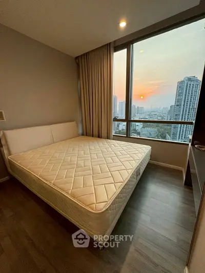 Modern bedroom with large window offering stunning city view at sunset.