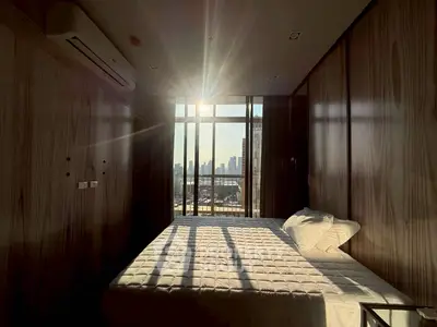 Modern bedroom with city view and natural light, featuring sleek wooden paneling and a comfortable bed.