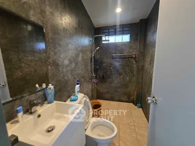 Modern bathroom with sleek dark walls, shower, and compact sink in a stylish home.