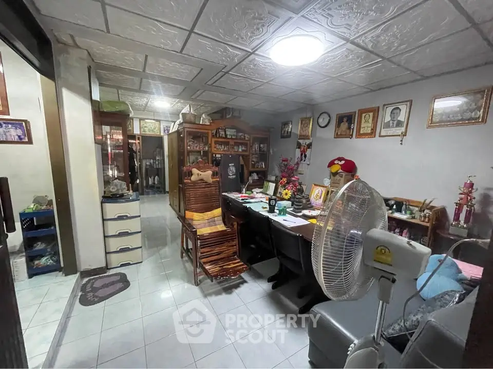 Cozy living room with traditional decor and ceiling tiles, featuring a fan and wooden furniture.
